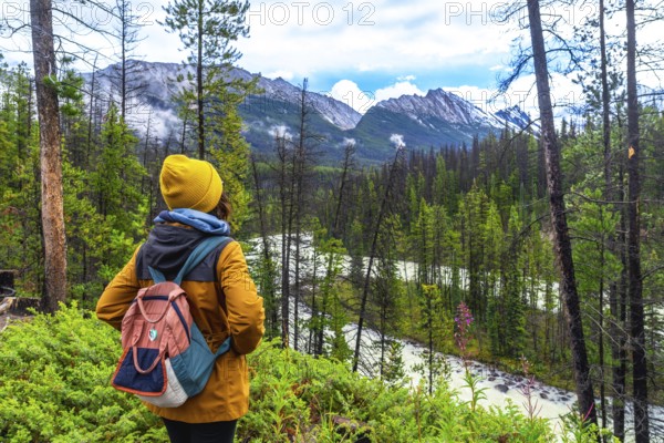 Female hiker with backpack enjoying the breathtaking view of sunwapta falls and the majestic canadian rockies in jasper national park, alberta, canada, surrounded by lush green forest