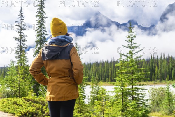 Tourist enjoying breathtaking view of majestic, cloud shrouded mountains and serene lake along icefields parkway in the canadian rockies, alberta, embodying tranquility and wanderlust