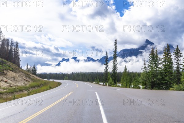 Scenic highway winds through a majestic mountain range, offering breathtaking views of the canadian rockies, under a cloudy sky, in alberta, canada