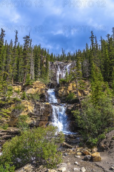 Water cascading over rocky cliffs at tangle creek falls in jasper national park showcases nature's power and beauty, surrounded by lush evergreen forest under a partly cloudy sky