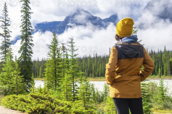 Pausing to admire breathtaking views of majestic mountains, serene lakes, and lush pine forests, a hiker embraces the tranquility of nature along the icefields parkway