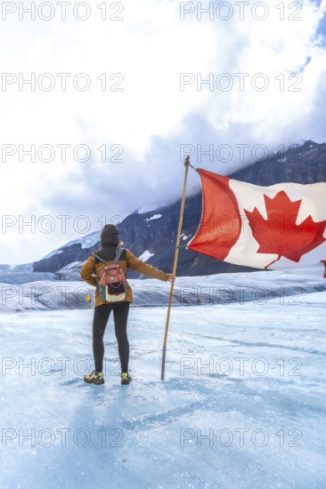 Tourist is holding large canadian flag while standing on athabasca glacier in jasper national park, a popular tourist destination in the canadian rockies known for its stunning natural beauty