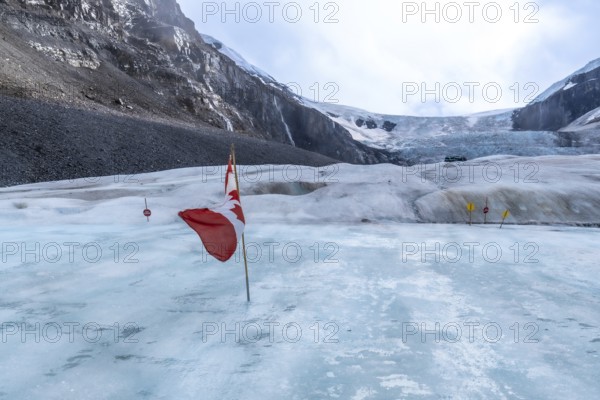 Canadian flag waving on the athabasca glacier, with traffic signs guiding a safe path through the icy landscape of jasper national park, alberta, canada
