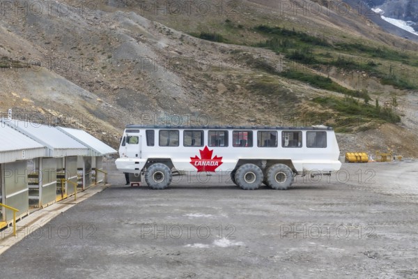Large all terrain ice explorer bus, adorned with a canadian flag, parked near athabasca glacier in jasper national park, highlighting sustainable tourism in the rockies