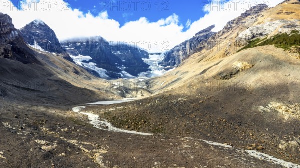 Melting athabasca glacier reveals rocky terrain beneath, creating a striking brown and white landscape against a vibrant blue sky with fluffy clouds in jasper national park, alberta