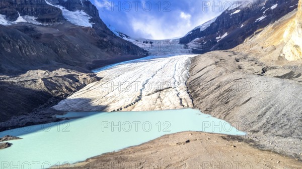 Athabasca glacier flows into a vibrant turquoise lake, showcasing the effects of climate change on the canadian rockies in jasper national park, alberta