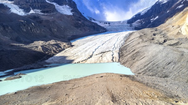 Athabasca glacier is melting into a vibrant turquoise lake, showing the effects of climate change in jasper national park, alberta, canada, on a sunny day with blue sky and white clouds