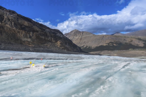 Yellow warning signs and red flags marking crevasses on the athabasca glacier illustrate the impact of climate change on this icy landscape in jasper national park, alberta
