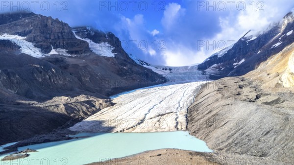 Athabasca glacier flows down from the columbia icefield, melting into a turquoise lake, surrounded by rugged mountains and a cloudy sky in jasper national park, alberta, canada