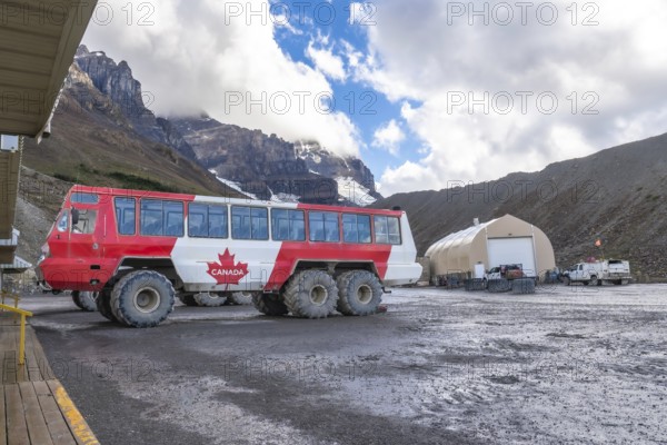 Large all terrain bus with a canadian flag parked near athabasca glacier in columbia icefield, offering stunning views of the glacier, mountains, and cloudy sky