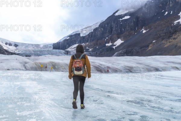 Tourist with a backpack walking across athabasca glacier in jasper national park, capturing the glacier's vastness and the breathtaking mountain landscape