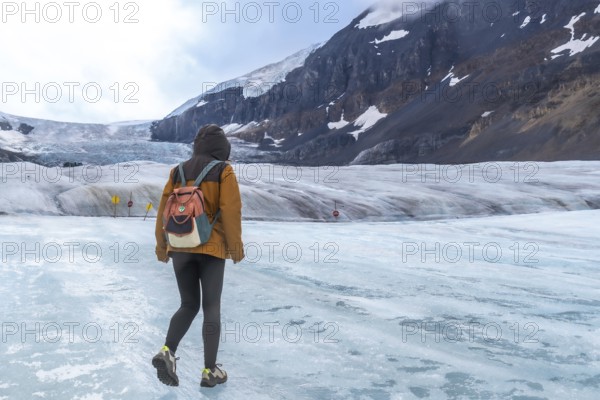 Tourist walking on the surface of athabasca glacier in jasper national park in the canadian rockies of alberta, canada, enjoying the stunning views of the mountains and ice formations