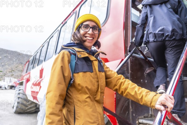 Smiling female tourist stepping off an ice explorer bus at athabasca glacier in jasper national park, enjoying a summer day trip in the canadian rockies