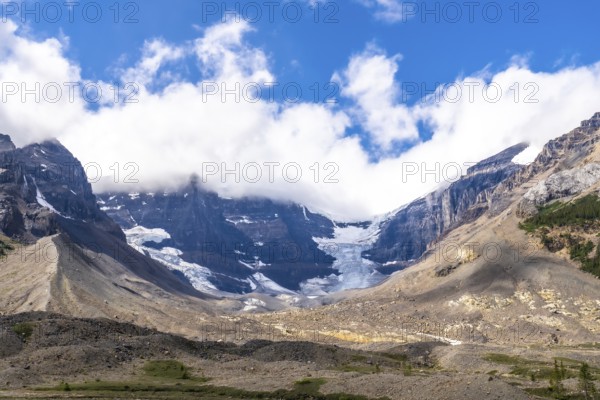 Athabasca glacier, part of the columbia icefield, reveals its shrinking beauty against the rugged canadian rockies in jasper national park, alberta, under a cloudy blue sky