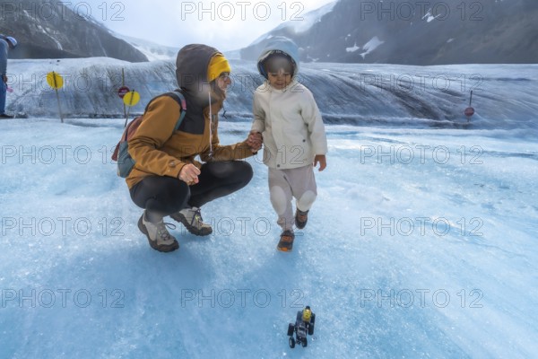 Mother and child enjoying playful moments on the athabasca glacier, with a toy vehicle in the foreground and the majestic canadian rockies in the background
