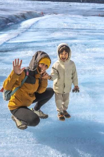 Mother and her son are enjoying their visit to the athabasca glacier in jasper national park, alberta, canada, waving and smiling amidst the stunning blue ice