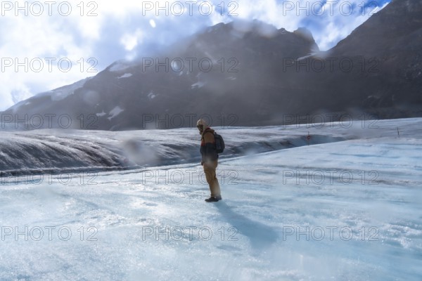 Hiker wearing winter clothing and a backpack, standing on the vast icy expanse of athabasca glacier in jasper national park, with rugged mountain peaks in the background