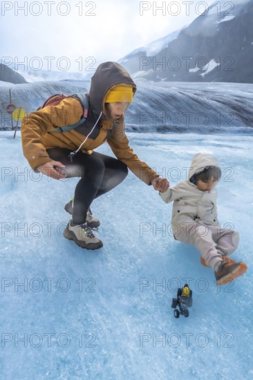 Tourist mother helping her child after slipping on the ice surface of the athabasca glacier in jasper national park, showcasing the beauty and potential hazards of glacial environments