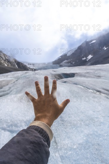 Tourist extends their hand towards the athabasca glacier, part of the columbia icefield in jasper national park, alberta, canada, experiencing the raw beauty and immensity of nature
