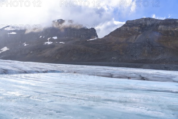 Tourists walking on the athabasca glacier in jasper national park, surrounded by mountains and clouds, emphasize the impact of climate change on glacial ice