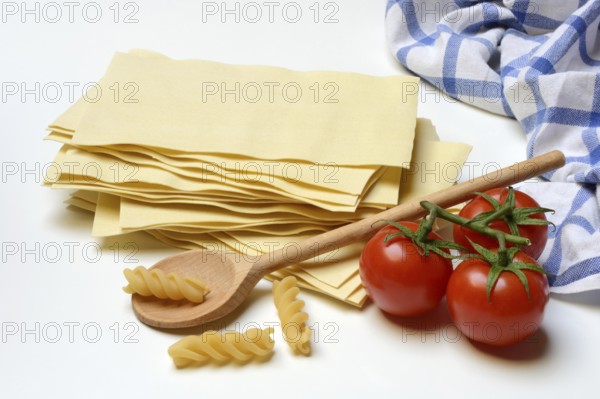 Lasagna, dried lasagna leaves and fusilli noodles with tomatoes and cooking spoon