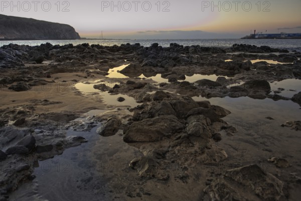 Rocks and puddles on the beach at sunrise, calm sea in the background, Los Cristianos Tenerife