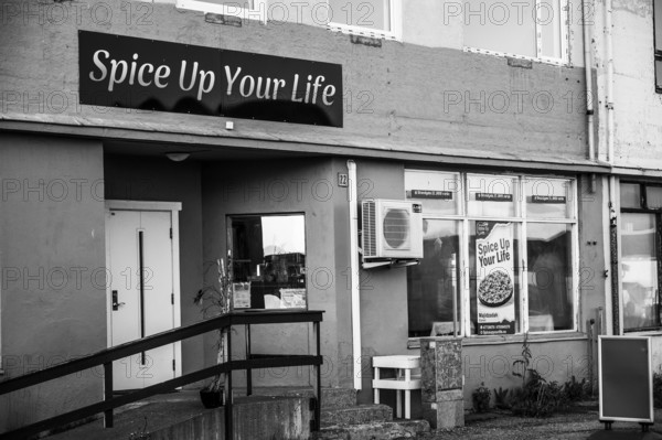 Exterior view of a restaurant with the sign 'Spice Up Your Life' in black and white, daisies (Leucanthemum)