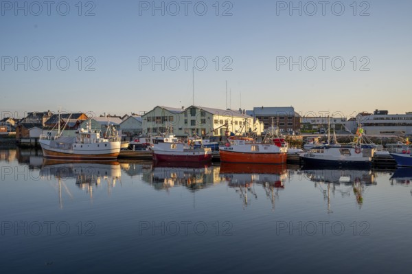 Harbour with several fishing boats in calm water, surrounded by buildings in the evening light, Vardø, Finnmark, Norway