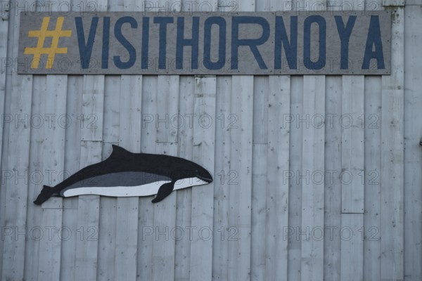 A whale image and a hashtag sign on a grey wooden wall with the slogan Visit Hornoya, Vardø, Finnmark, Norway