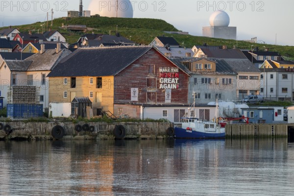 Houses and boats at a harbor against a green backdrop of hills in the evening light, Vardø, Finnmark, Norway