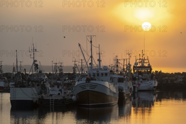 Fishing boats are moored in the harbor at sunset, the sea reflecting the warm colors of the sky, Vardø, Finnmark, Norway