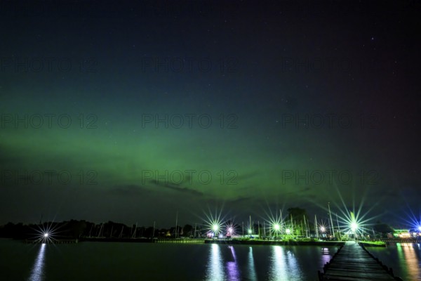 Glowing polar lights in shades of purple and green in front of an illuminated harbor on Lake Dümmer, Lembruch, Lower Saxony, Germany
