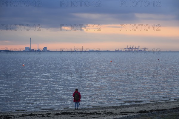 Person on the beach with a view of the sea and industrial areas in Wilhelmshafen right Jade-Weser Port, blue-orange twilight, Eckwarderhörne, Butjadingen, Lower Saxony, Germany