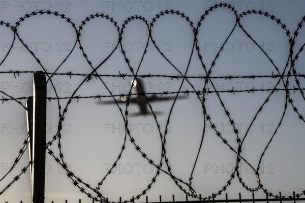 Symbolic picture security at the airport, outer fence at Düsseldorf International Airport, steel wire fence, with S-wire rollers, NATO wire, on the fence crown, airplane taking off, North Rhine-Westphalia, Germany