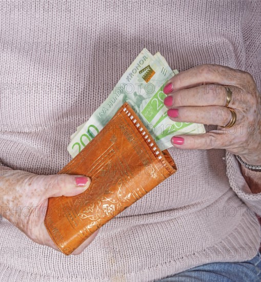 An elderly woman's hands take out Swedish banknotes from a wallet