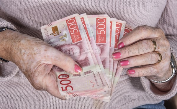 An elderly woman's hands holding Swedish 500-krona banknotes