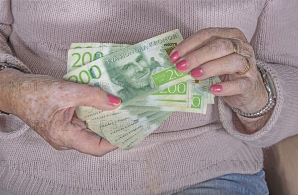 An elderly woman's hands holding Swedish 200-krona banknotes