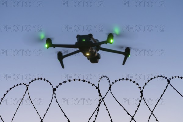 Symbolic picture, drone with glowing propellers over waves of barbed wire, airport, threat, espionage