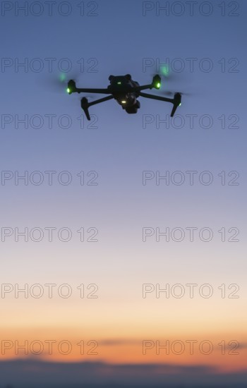 Drone floats in soft evening sky with green lights