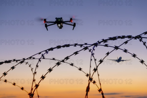 Symbolic picture, drone and airplane in the sky over barbed wire at sunset, airport, threat, espionage