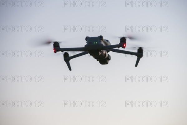 Flying drone with illuminated propellers at dusk