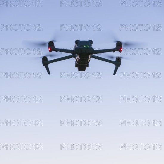 Drone with illuminated propellers floats against the evening sky