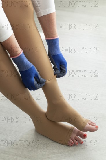 A woman sits at home and puts on medical compression stockings with special gloves on
