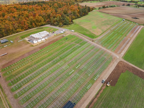 Solar frame on a field near an autumn forest and industrial site, Energiewende, construction of PV open space, Baden-Württemberg, Germany