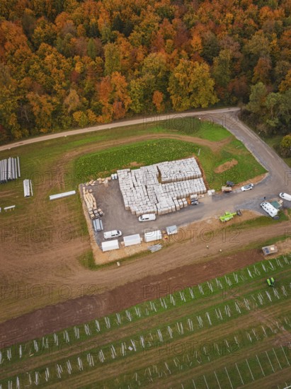 Autumn aerial view of a building materials warehouse with surrounding fields and an adjacent road, Energiewende, construction of PV open space, Baden-Württemberg, Germany
