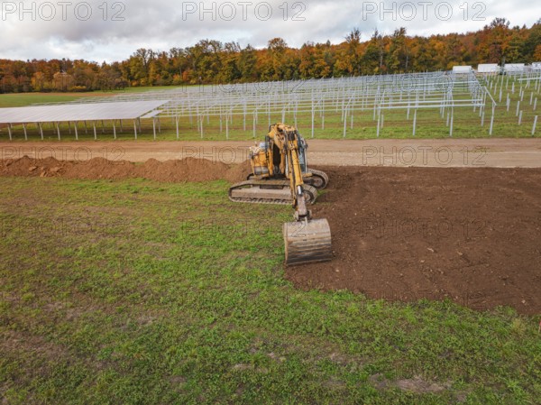 Excavator working near solar panel structures with autumn leaves in the background, energy revolution, construction of PV open space, Baden-Württemberg, Germany