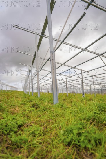 Close-up of metallic solar frames in the construction phase on a green field under cloudy sky, Energiewende, construction of PV open space, Baden-Württemberg, Germany