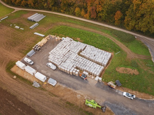 Warehouse with building materials and vehicles, surrounded by fields and an asphalted road, energy transition, construction of PV open space, Baden-Württemberg, Germany