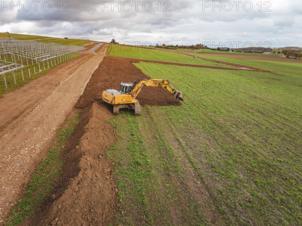 Yellow excavator shovels soil and redesigns the field, energy transition, construction of PV open space, Baden-Württemberg, Germany