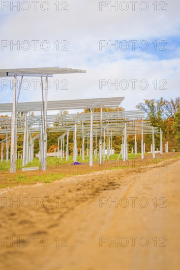 Unpaved road leads past metal structures for solar panels under blue sky, Energiewende, construction of PV open space, Baden-Württemberg, Germany
